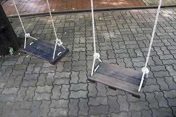 Lonely, nostalgic view of an empty wooden swing in quiet park. This outdoor scene on stone pavement evokes feeling of waiting and forgotten childhood memory