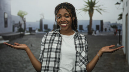 Woman showing palms up gesture with both hands on a cobblestone street wearing white tee and plaid shirt; contemplation.
