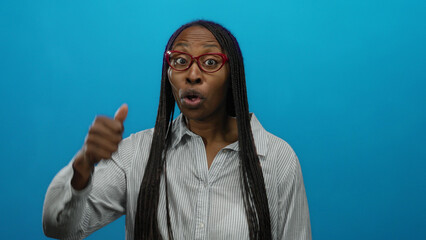 Woman smiling in striped shirt with bright glasses and expressive gestures against an isolated blue wall shows confidence and joy.