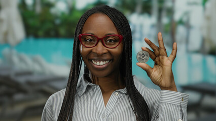 Woman smiling holding ethereum coin by pool at resort showcasing crypto confidence in outdoor setting.