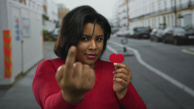 Young woman holding red paper heart on city street, symbolizing love and confidence.