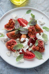 Salad with fresh tomatoes, torn fig fruits and cottage cheese on a white plate, vertical shot, middle close-up