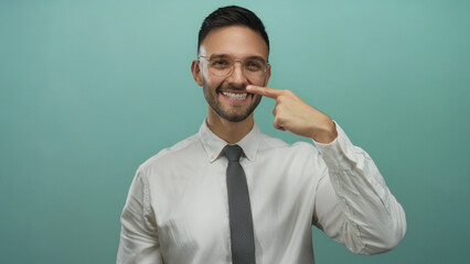 Young man smiling and pointing to his nose against a blue background wearing a white shirt and tie expressing humor and confidence