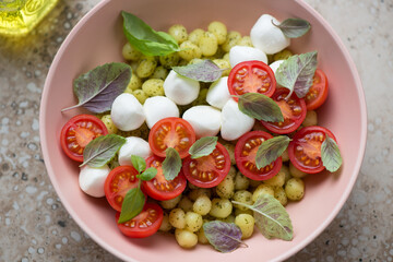 Italian mini potato gnocchi with cherry tomatoes, mozzarella balls and basil in a roseate bowl, horizontal shot, middle close-up