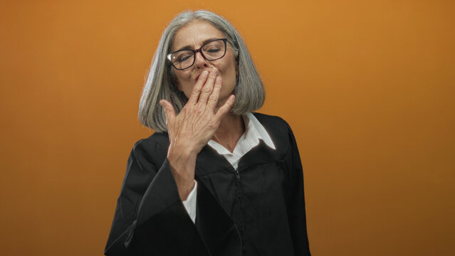 Middle aged grey haired woman judge blowing a kiss with hand in orange studio; pride achievement recognition milestone. - Powered by Adobe