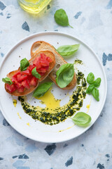 White plate with tomato bruschettas and basil oil, vertical shot on a white and blue granite background, high angle view