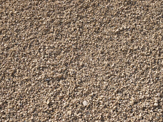 Close-up of small beige gravel stones creating a natural rough surface texture in daylight