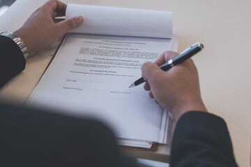 Businessman reviewing and signing official documents at a desk, representing contract approval,...