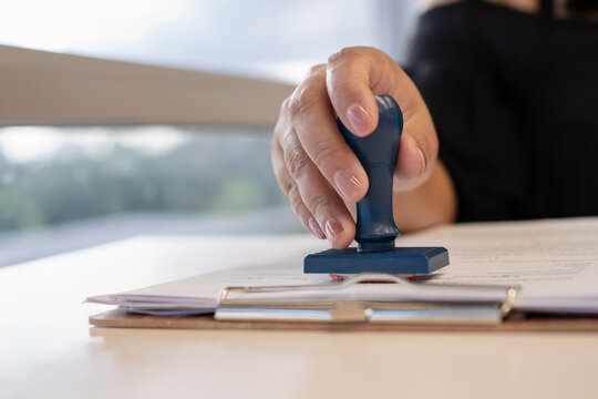Close-up of a businessperson stamping a contract document, symbolizing approval, legal agreement, successful deal, authorization, and official corporate paperwork process.