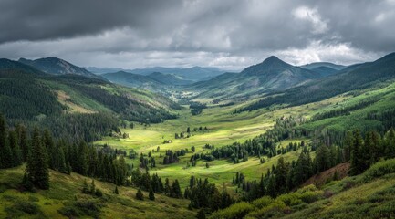 Fototapeta premium Mountain valley panorama under a stormy sky. Lush green meadows and forests nestled between rugged peaks