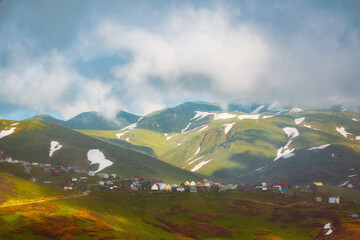 Naklejka premium Aerial view of Gomis Mta in Georgia, a mountain village with small wooden houses surrounded by snow and green hills. Peaceful and scenic highland landscape