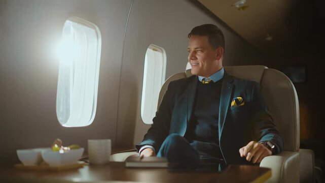 Confident mature businessman relaxing in a luxury airplane seat, enjoying a comfortable first-class flight and smiling while looking out the window during his business travel