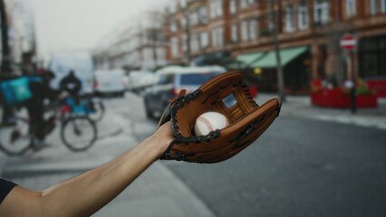 Man holding baseball glove with ball on urban street, showcasing city life with delivery cyclists and vehicles in the background.