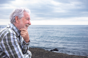 Happy senior man outdoors near the ocean, smiling and enjoying a peaceful moment by the sea. The elderly bearded man looks relaxed and content, expressing positivity, freedom, and active aging.