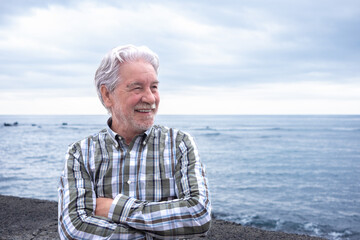 Happy senior man outdoors near the ocean, smiling and enjoying a peaceful moment by the sea. The elderly bearded man looks relaxed and content, expressing positivity, freedom, and active aging.