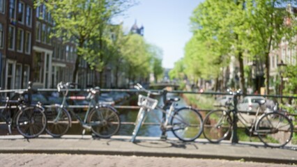 Bicycles parked against a railing on a sunny day with a defocused backdrop of amsterdam's vibrant canals and green trees.