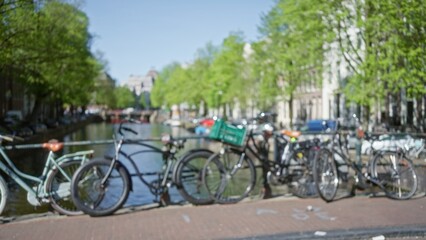 Blurred bicycles parked along amsterdam canal with bokeh background and green trees under clear blue sky.