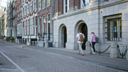 Blurred figures walking along a historic amsterdam street with brick and stone buildings lining the...