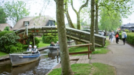 Blurred image captures people strolling near the idyllic canals of giethoorn with lush greenery and quaint homes in the netherlands creating a serene atmosphere.