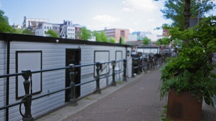 Blurred view of a houseboat along an amsterdam canal with a defocused background of urban architecture and greenery under a clear blue sky.