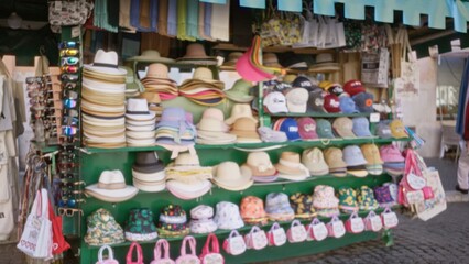 Market hat stall blurred bokeh street scene with stacked hats, caps and hanging bags in soft defocused focus; background backdrop copyspace calm.