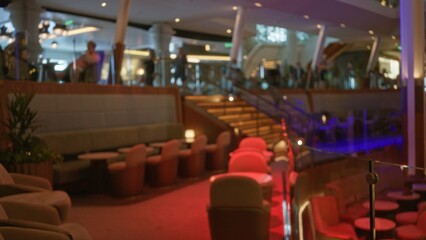 Lounge seating area with stairs, tables and soft red lighting in blurred bokeh interior; background...