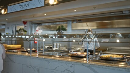 Buffet counter interior with soft defocused foreground and shallow bokeh, stainless steel serving trays and marble counter in a cafe; background backdrop copyspace calm.
