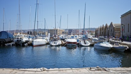 Fototapeta premium Boats and sail masts clustered along a sunlit marina quay, soft blurred bokeh focus with defocused water reflection outdoor; background backdrop copyspace calm.