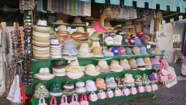 Market hat stall blurred bokeh street scene with stacked hats, caps and hanging bags in soft defocused focus; background backdrop copyspace calm. - Powered by Adobe
