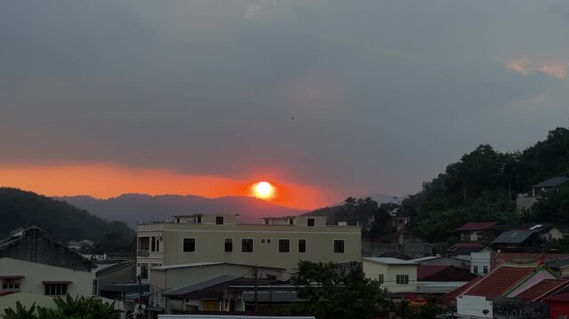 Static shot from a hilltop showing a large red sun disk setting over the rural landscape and horizon at Titi Village, Malaysia.