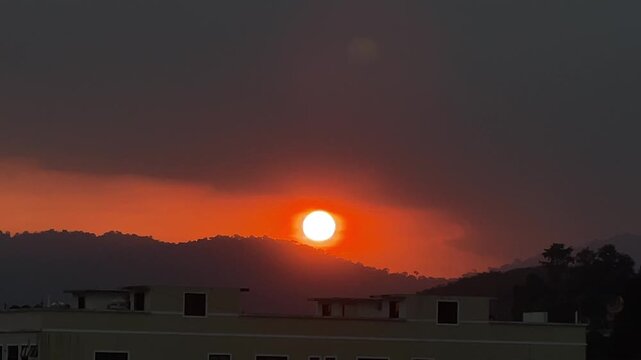 Static shot from a hilltop in Titi Village Malaysia showing a bird flying across a large red sun disk during a golden sunset.