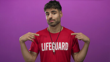 Young hispanic lifeguard man in red shirt pointing finger at silver whistle in studio setting;...