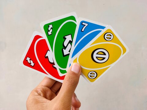 Malang, Indonesia - November 02, 2025: A hand holds a fanned-out selection of colorful Uno cards, including a red reverse, green reverse, blue 7, and yellow skip card.