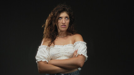Fototapeta premium Woman with arms crossed and exposed shoulders in studio against black backdrop; defiance resilience.