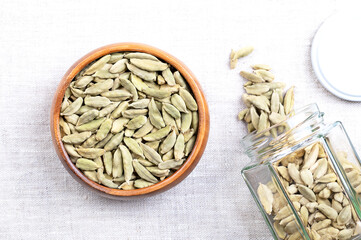 Whole, dried cardamom pods, in a wooden bowl on linen. Sometimes called cardamon, or cardamum, greenish fruits with seeds of Elettaria cardamomum, a spice with sharp, strong and punchy aroma.