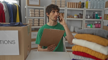 Man holds clipboard and talks on phone inside a building donation center amid stacked clothes and boxes on shelves; compassion.