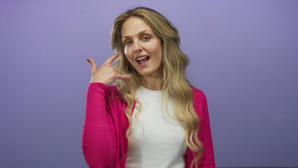 Young blonde woman gestures playfully with a hand gesture mimicking a phone call against an...