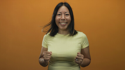 Obraz premium Young hispanic woman with clenched fists and visible hands in studio with orange backdrop, smiling and animated; joy triumph.