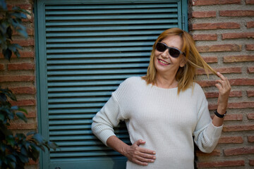Mature woman smiling wearing sunglasses against wall