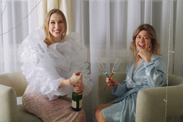 two friends dressed up in fancy clothes open a bottle of sparkling wine