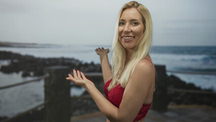 Woman smiling broadly pointing hands toward sunlit ocean waves on rocky beach; serenity and freedom.