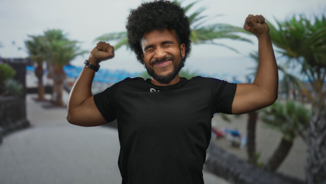 Smiling man in staff uniform joyfully stretching by the seaside with palm trees in the background on a cloudy day. - Powered by Adobe