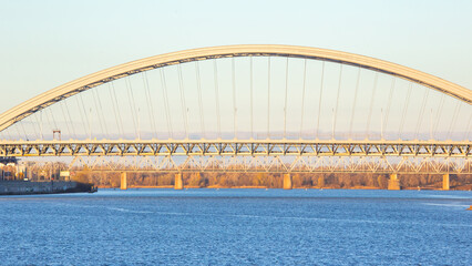 Clear evening view of a large arch bridge spanning a river with calm water reflections