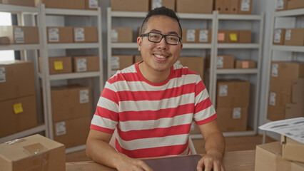 Man typing on laptop amid stacked parcels and shipping labels in a delivery office building with...
