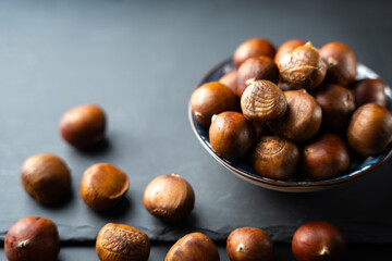 Fresh raw chestnuts in a bowl on black background, healthy organic autumn food, natural seasonal nut rich in flavor and nutrition, perfect ingredient for cooking and roasting.