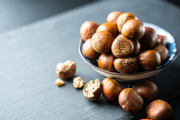 Fresh raw chestnuts in a bowl on black background, healthy organic autumn food, natural seasonal nut rich in flavor and nutrition, perfect ingredient for cooking and roasting.