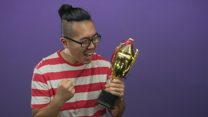 Man holding a gold trophy and pumping fist while cheering in a purple studio with a striped shirt;...