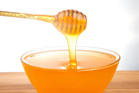 Golden honey dripping from a wooden dipper into a glass bowl