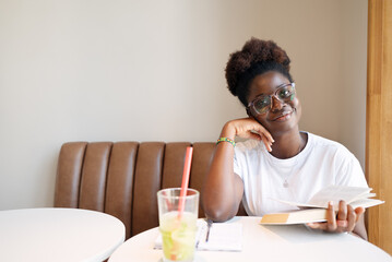 Young woman reading a book and taking notes in a bright modern cafe, symbolizing education, learning, personal growth, mindfulness and inspiration in everyday life.