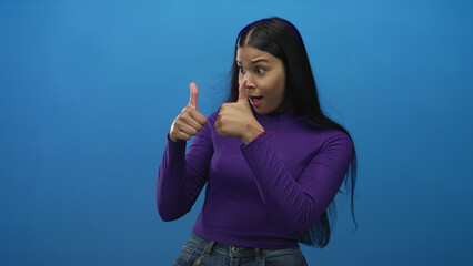 Woman wearing purple long sleeve top and denim jeans and pointing both index fingers in studio;...